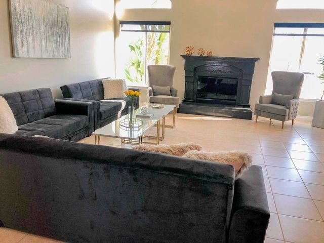 Modern living room with dark sectional sofas, glass coffee table, fireplace, and bright windows