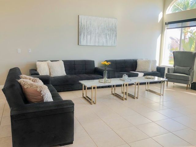 Modern living room with black sectional sofas, glass coffee tables, and beige tile flooring