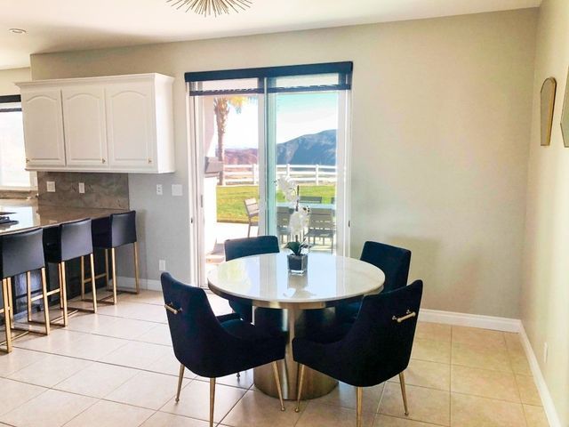 Bright dining area with a round glass table, dark chairs, kitchen counter, and sliding doors to a patio.