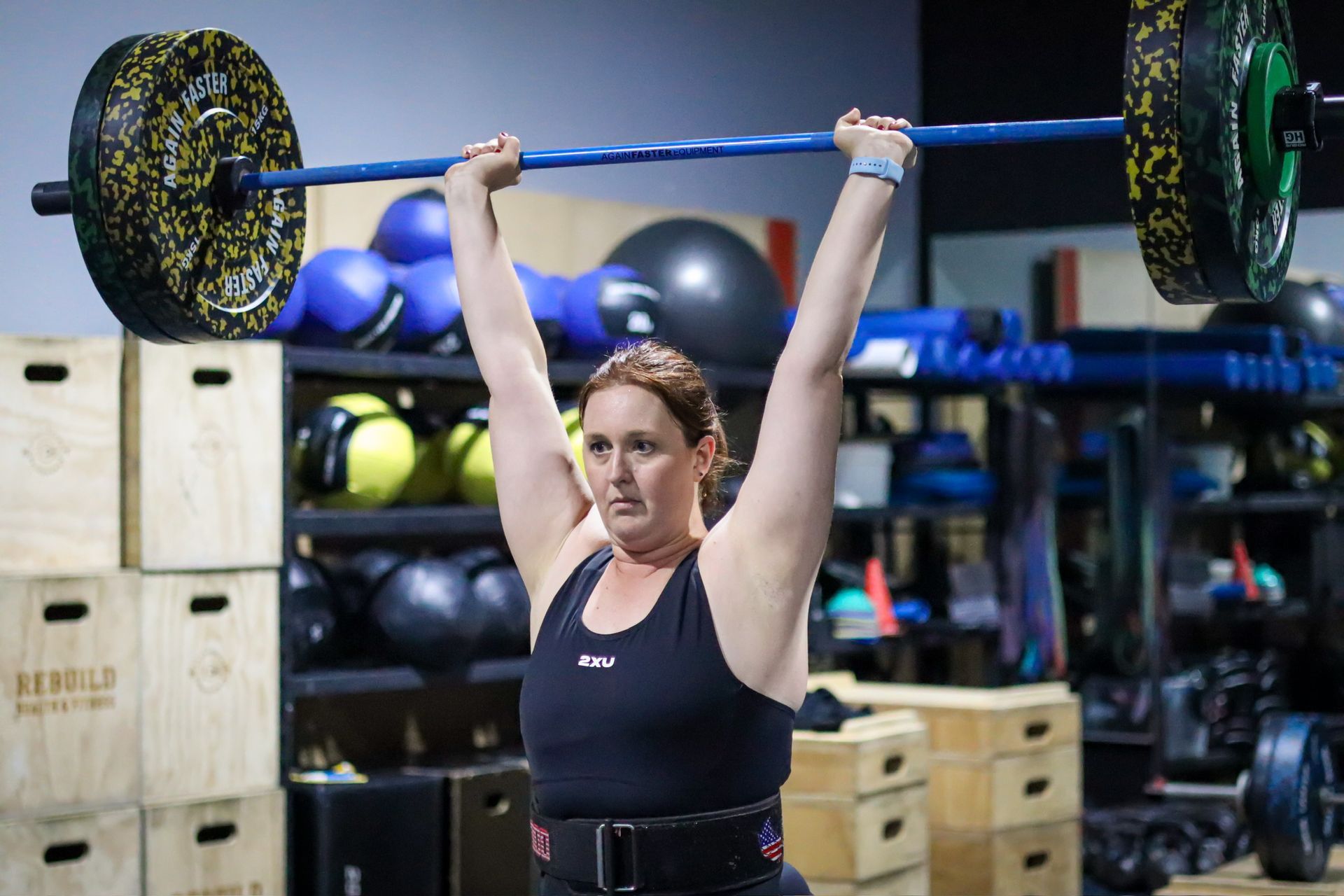 A woman is lifting a barbell over her head in Rebuild Health and Fitness in Wynnum West & Capalaba, QLD
