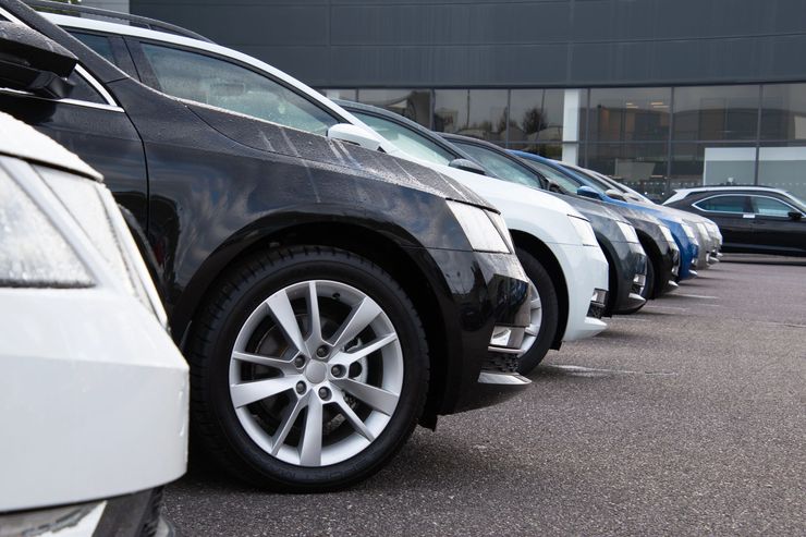 Una fila di auto parcheggiate nel piazzale di una concessionaria, con un SUV nero in primo piano e un edificio moderno sullo sfondo.