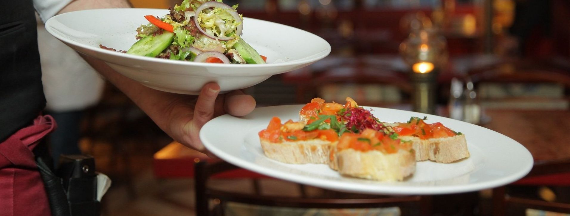 A waiter is carrying two plates of food in a restaurant.