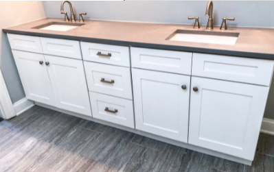 White bathroom vanity with double sinks, brass faucets, and gray wood-look floor tiles