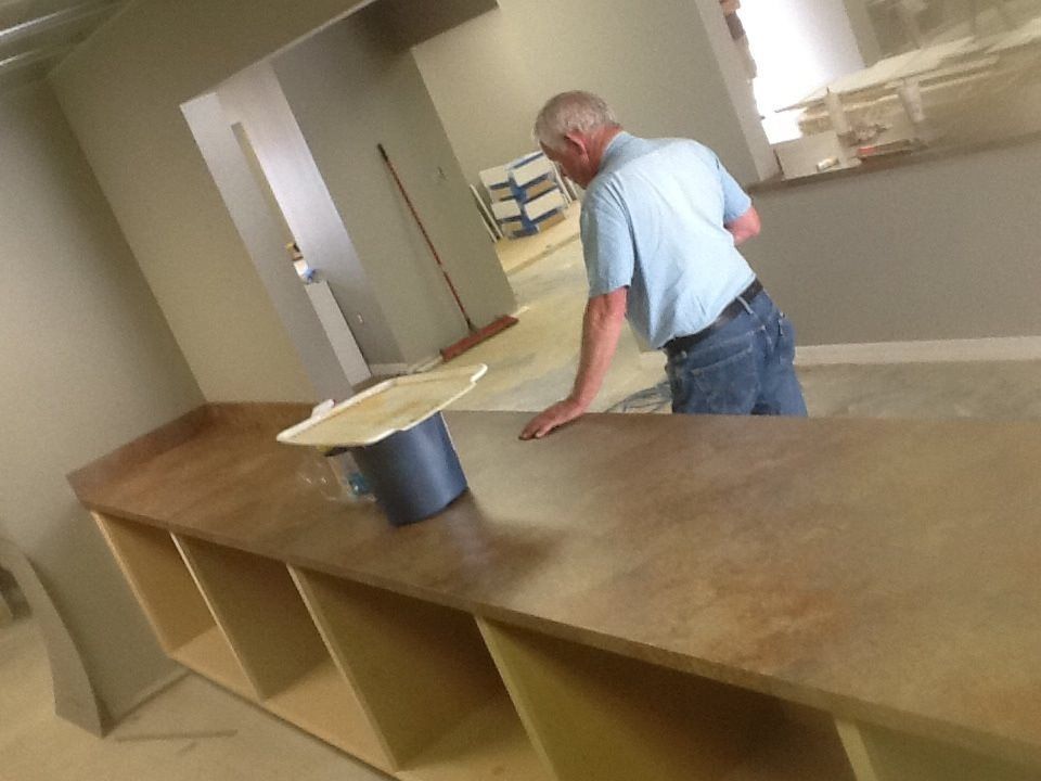 Man in blue shirt cleaning a long wooden counter in a sparse room