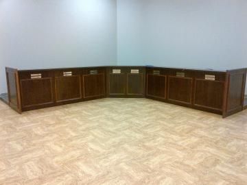 Empty room with curved dark wood counters against gray walls and a light patterned floor