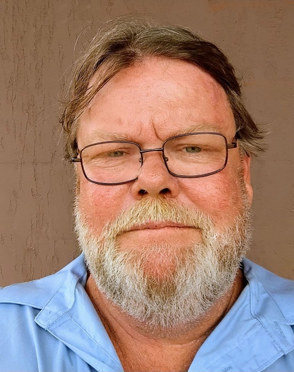Man with glasses and gray beard, wearing a blue shirt, looking at the camera.