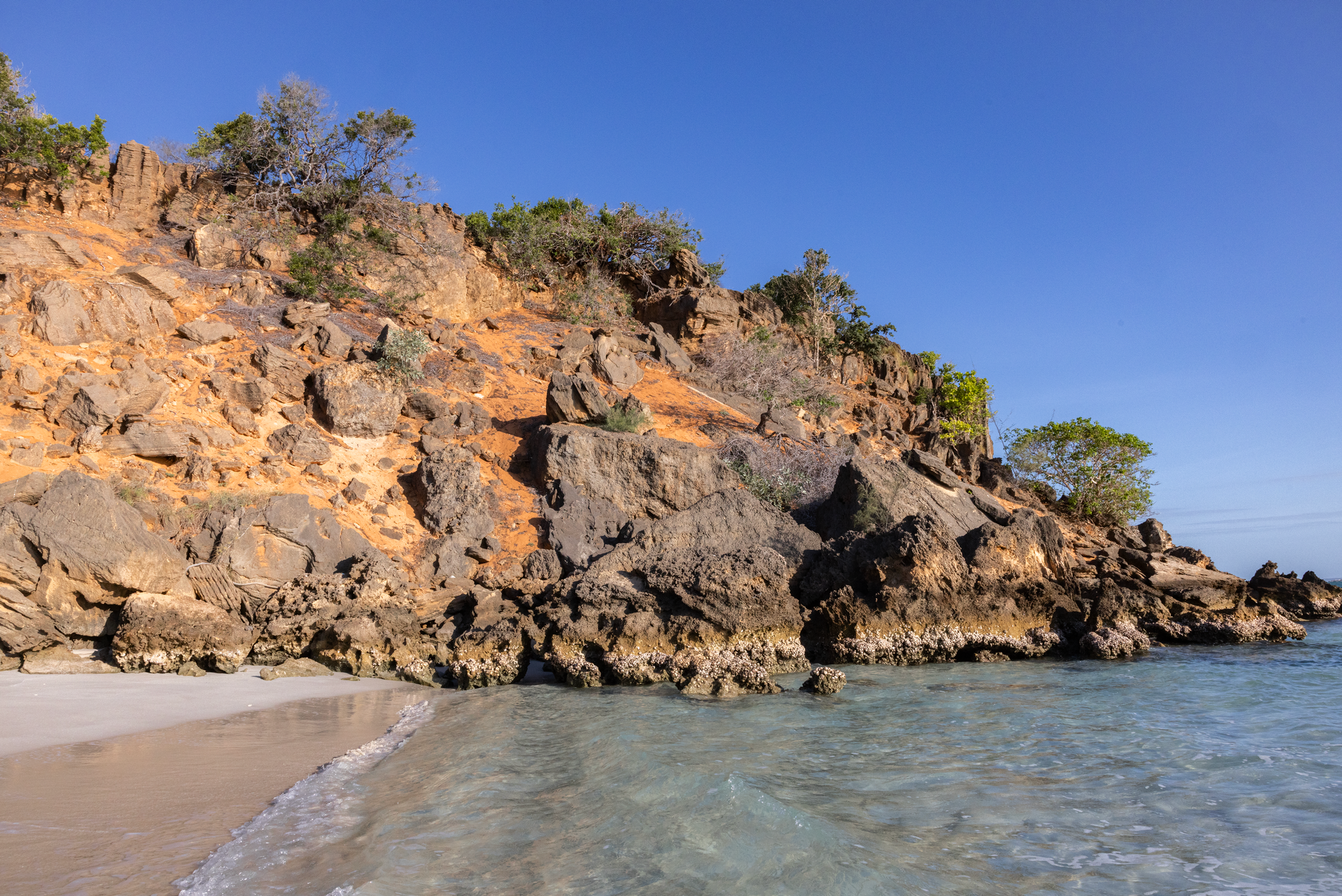 Rocky coastal cliff beside a calm blue sea under a clear sky