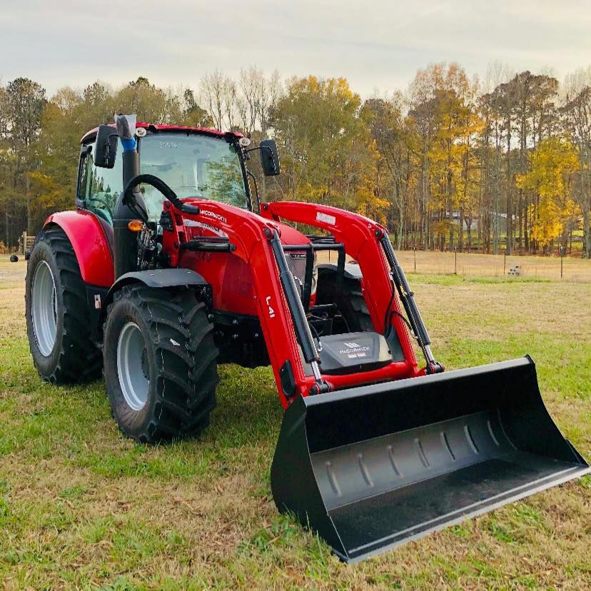 A red tractor with a black bucket is parked in a grassy field.