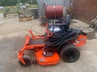 An orange and black lawn mower is parked in a parking lot.