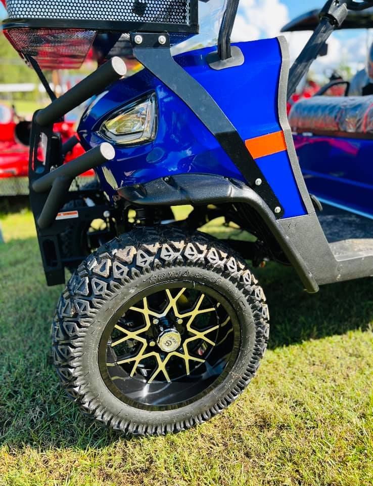A blue golf cart with black and yellow wheels is parked in the grass.