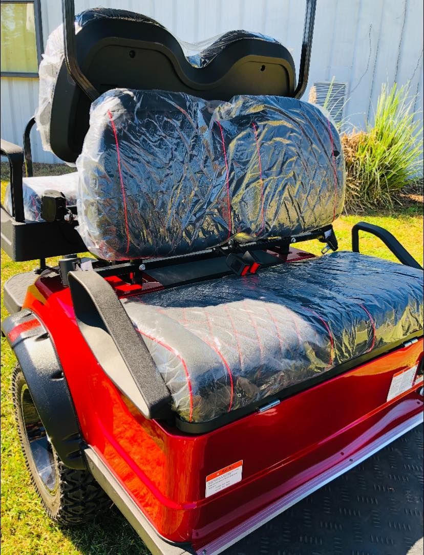 A red golf cart with black seats is parked in the grass.