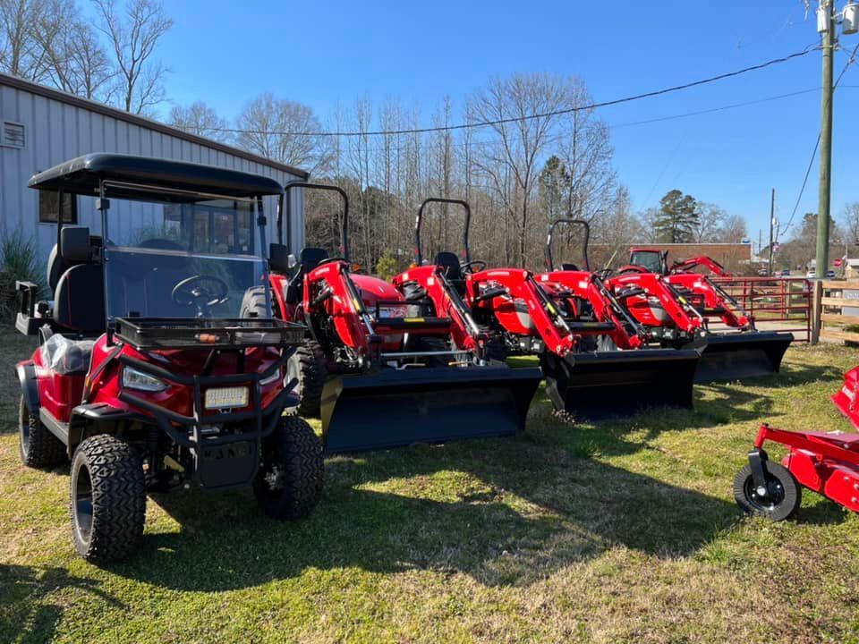 A row of red golf carts and tractors are parked in a grassy field.
