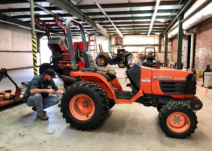 A man is working on a small orange tractor in a garage.
