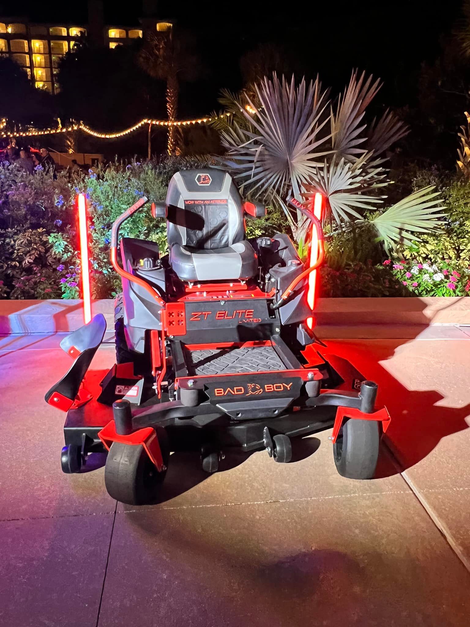 A red and black lawn mower is parked on a sidewalk at night.