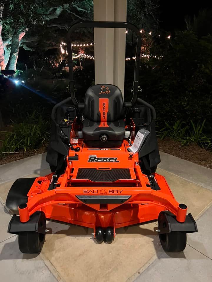 An orange and black lawn mower is parked on a sidewalk.