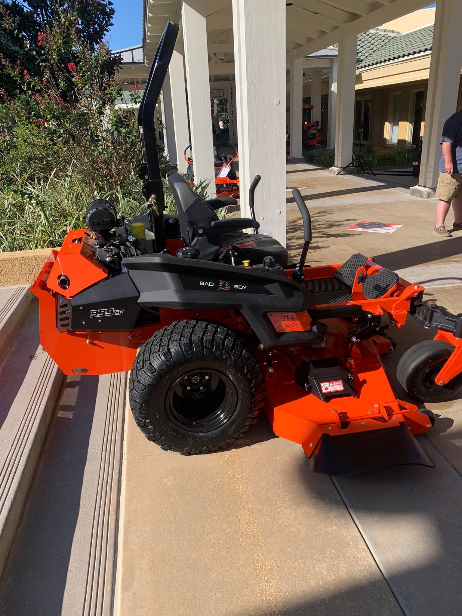 An orange and black lawn mower is parked on the sidewalk next to a building.