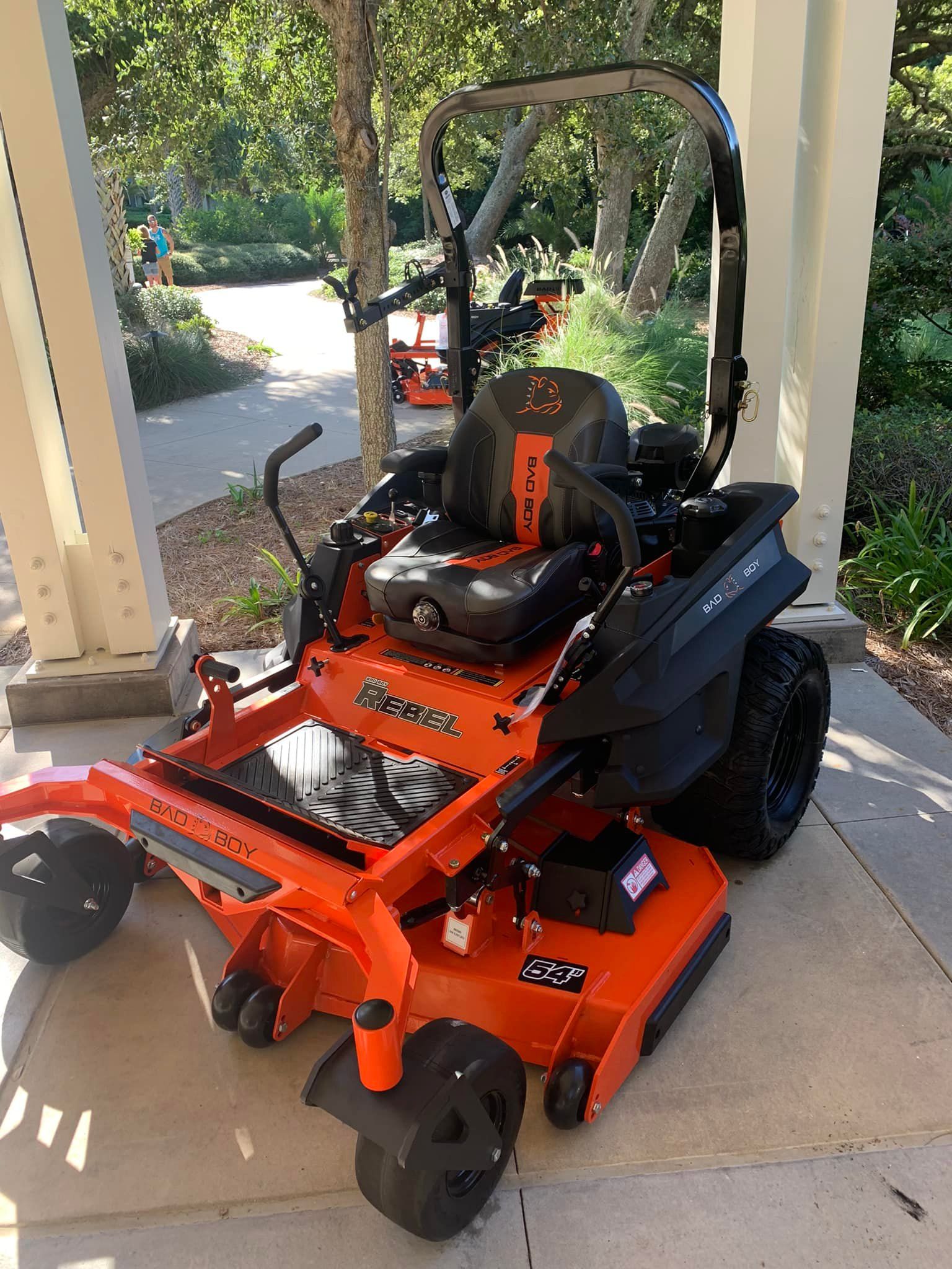 An orange and black lawn mower is parked under a porch.