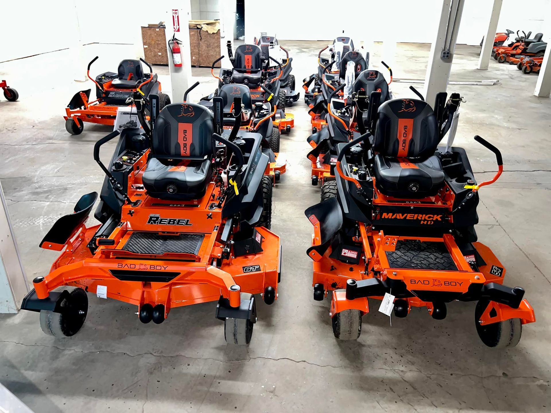 A row of orange and black lawn mowers are lined up in a warehouse