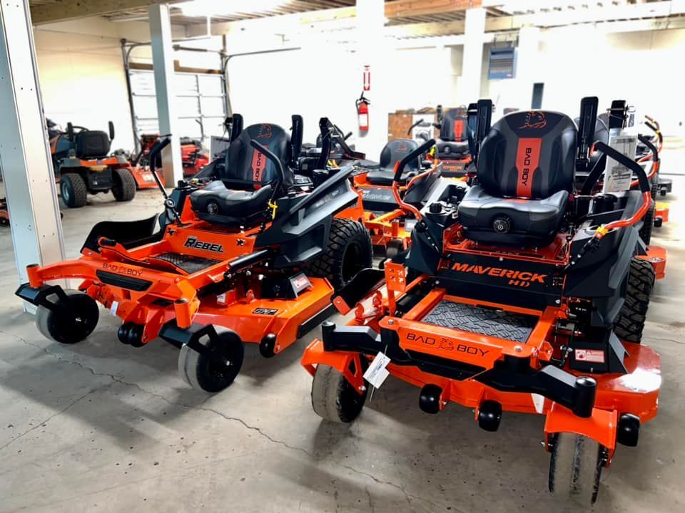 A row of orange and black lawn mowers are parked in a garage.