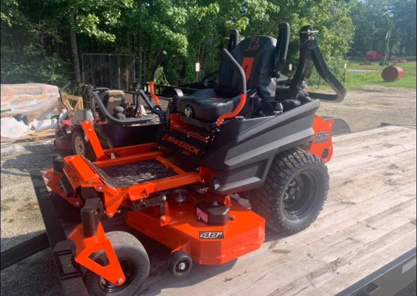 An orange and black lawn mower is parked on a trailer.
