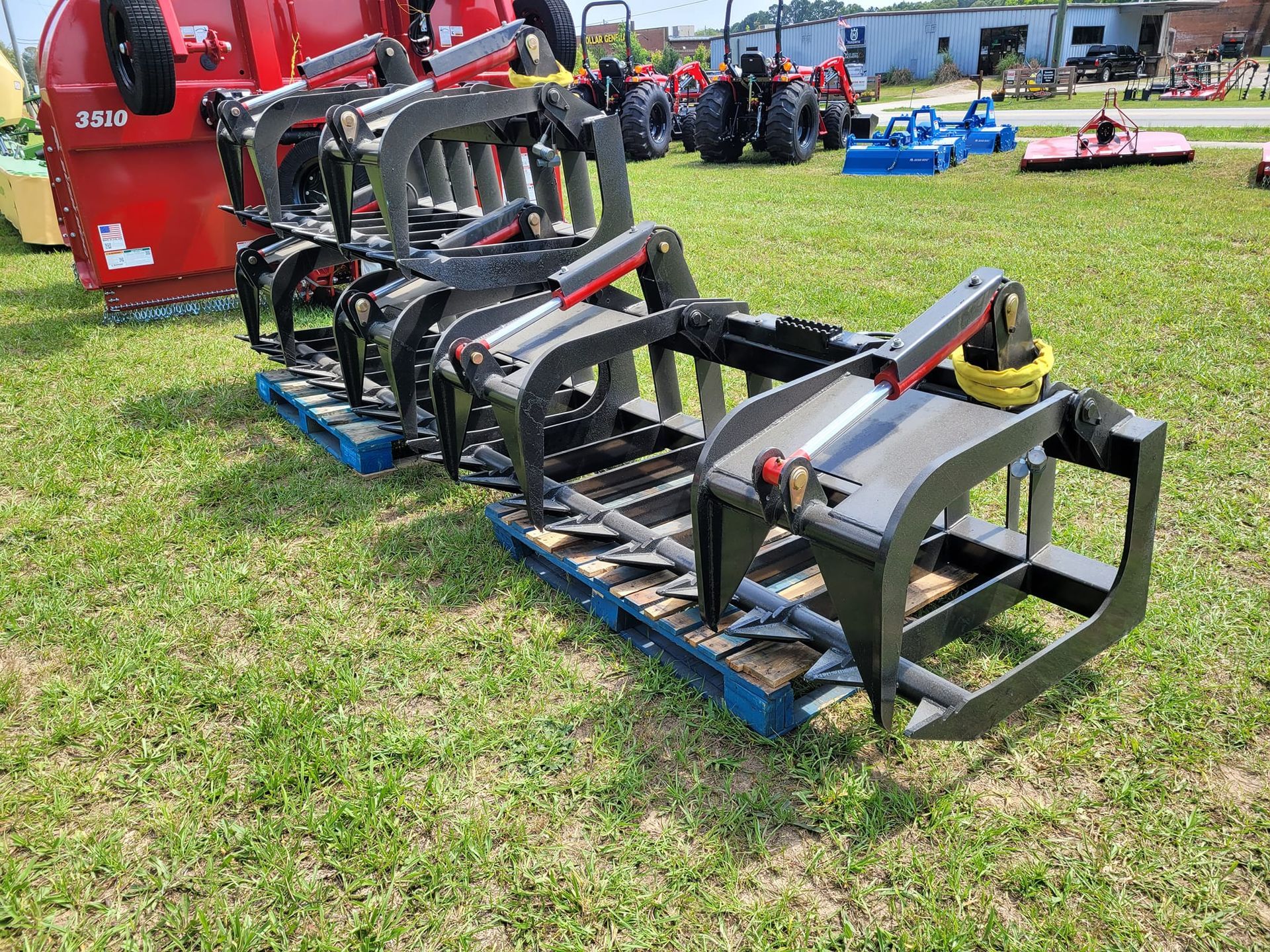A row of tractor grapple hooks sitting on top of a pallet in a grassy field.