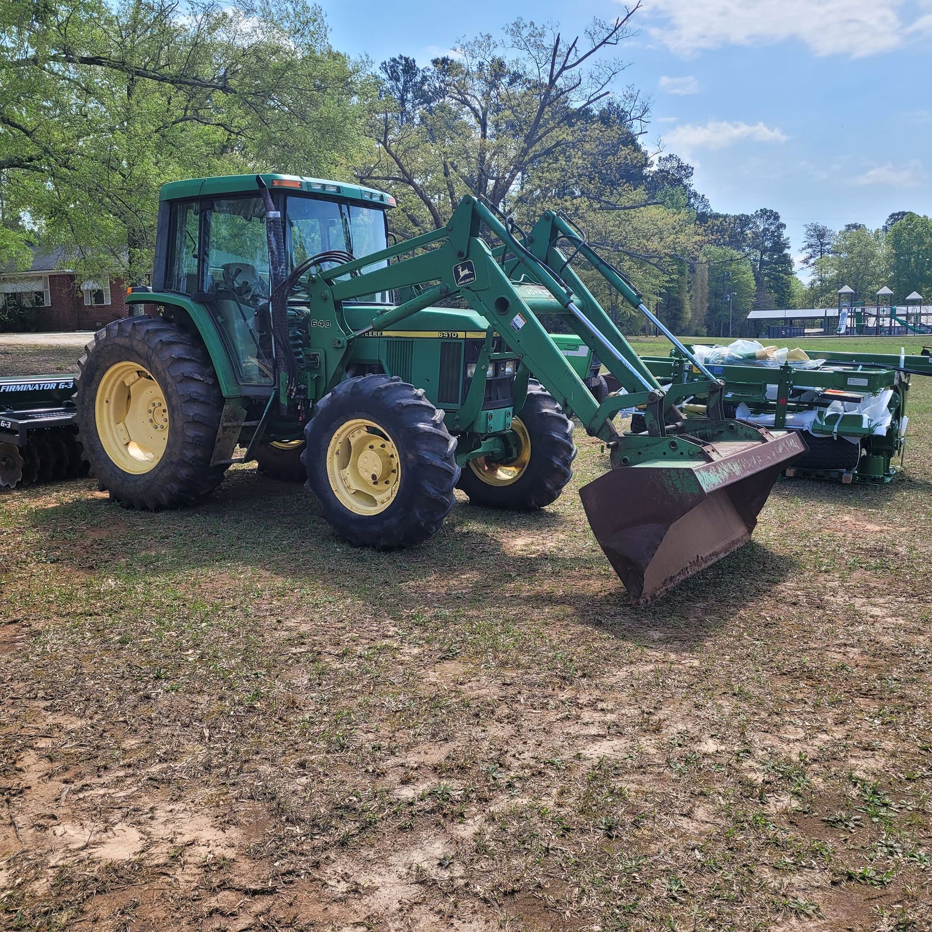 A green tractor with a bucket attached to it is parked in a field.