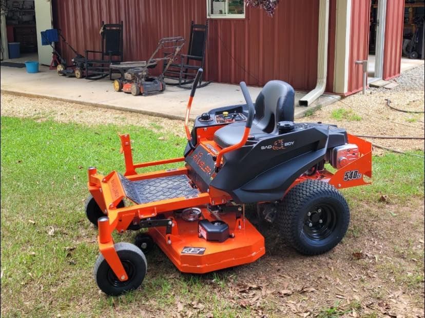An orange lawn mower is parked in front of a red building