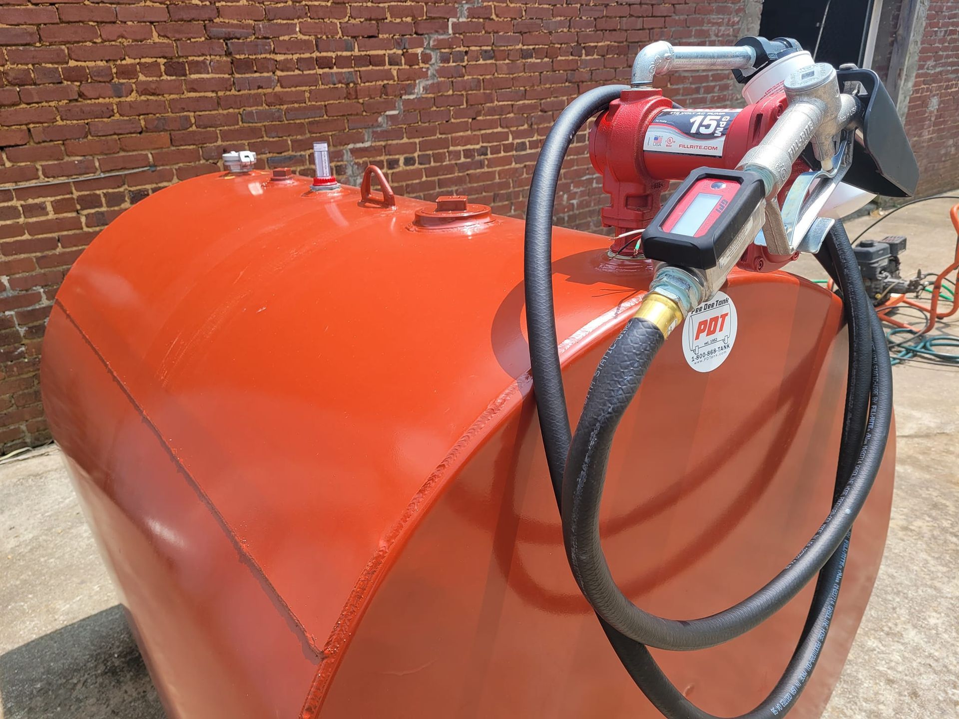 A red tank with a pump attached to it is sitting in front of a brick building.
