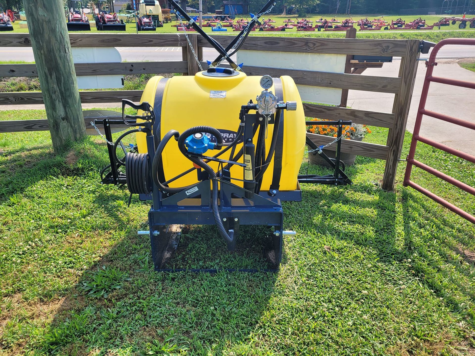 A yellow sprayer is parked in the grass next to a fence.
