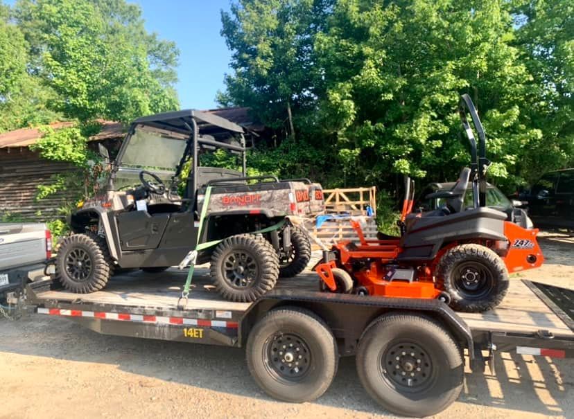 A trailer with a utility vehicle and a lawn mower on it.
