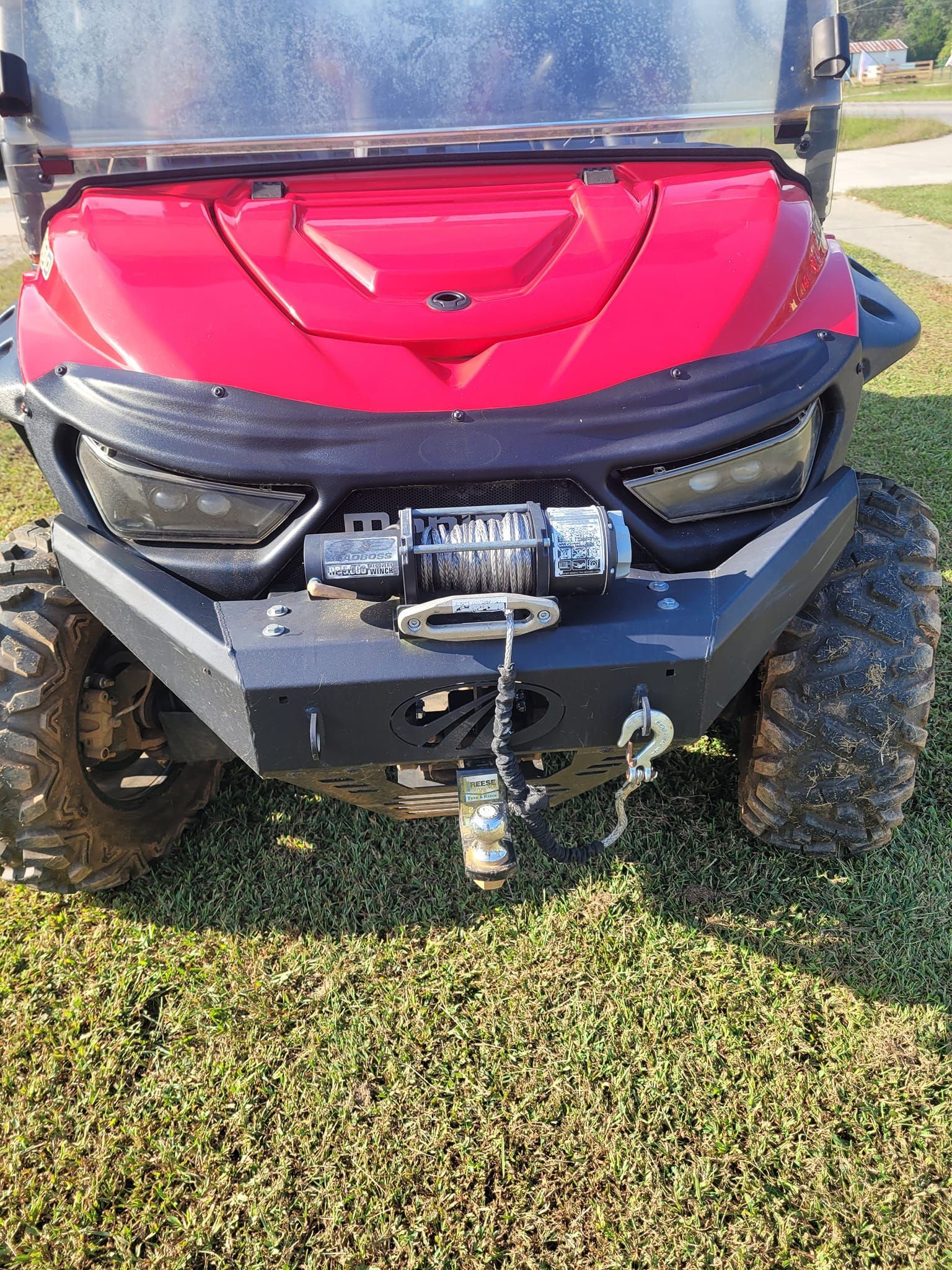 The front of a red golf cart is parked in the grass.