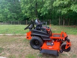 An orange and black lawn mower is parked in a grassy field.