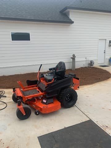 An orange and black lawn mower is parked in front of a house.