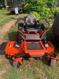 A red and black lawn mower is parked in the grass.