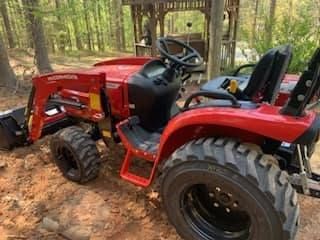 A red tractor is parked in the dirt in the woods.