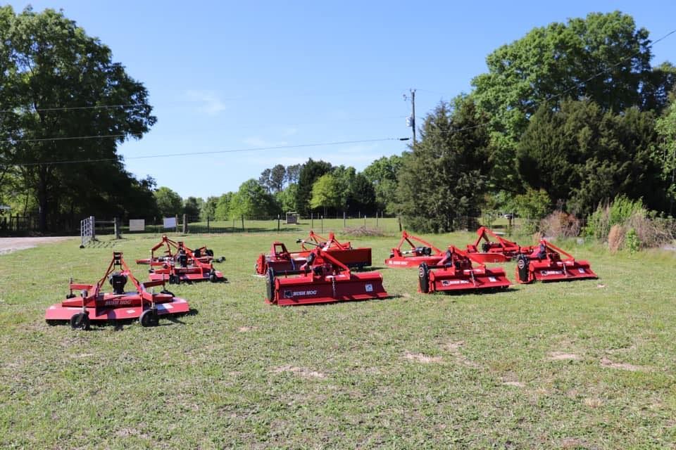 A row of red lawn mowers are sitting in a grassy field.