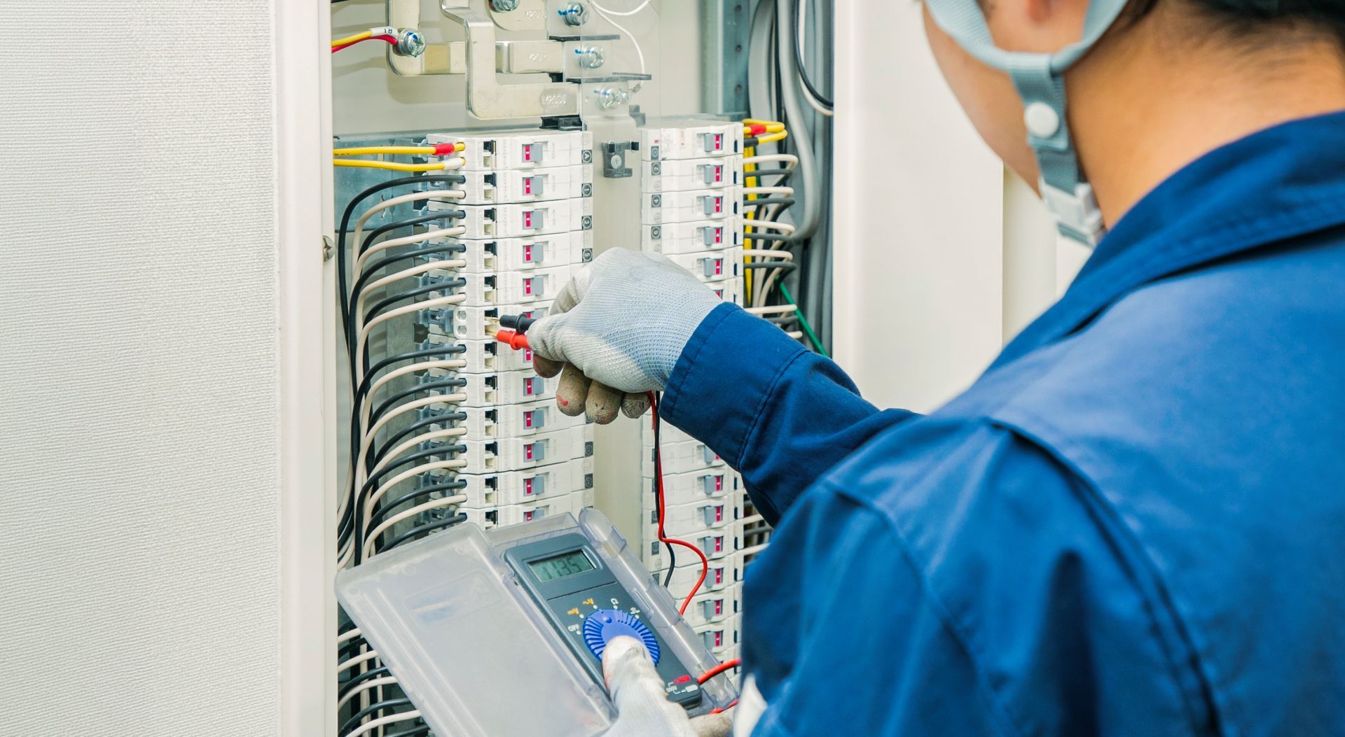 Technician inspecting electrical control panel with a tablet, wearing blue uniform and gloves