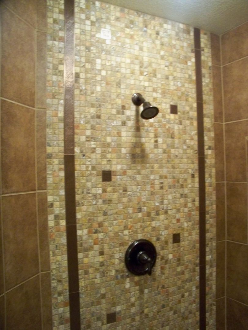 A shower with a tiled wall and a shower head.