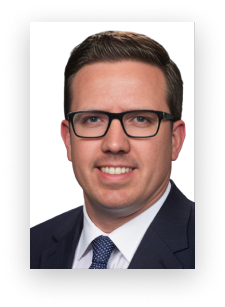 A man wearing glasses and a suit smiles for the camera