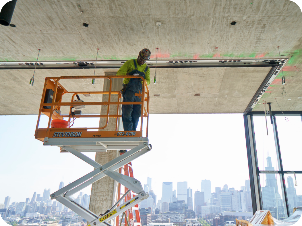 A man is standing on a scissor lift with a city skyline in the background