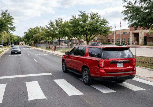 Red GMC Yukon driving through a marked crosswalk near a school
