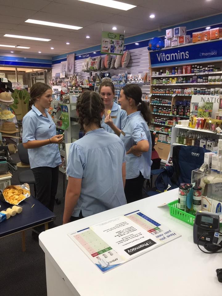 Employees in blue shirts talk in a vitamin aisle of a store.