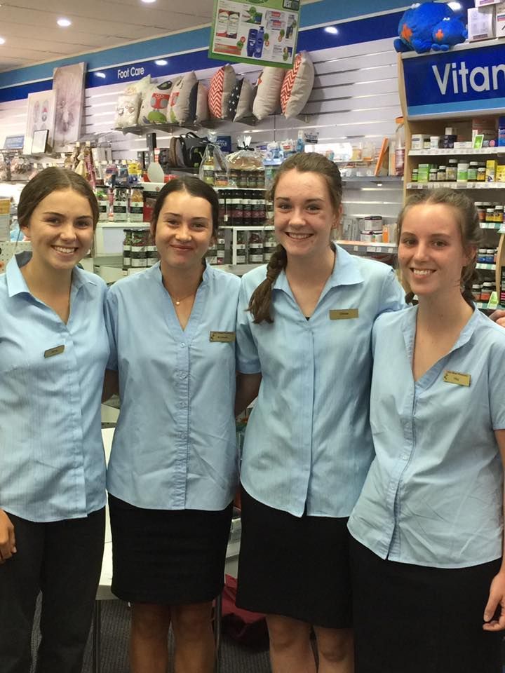 Four store employees in light blue uniforms smiling in a retail aisle