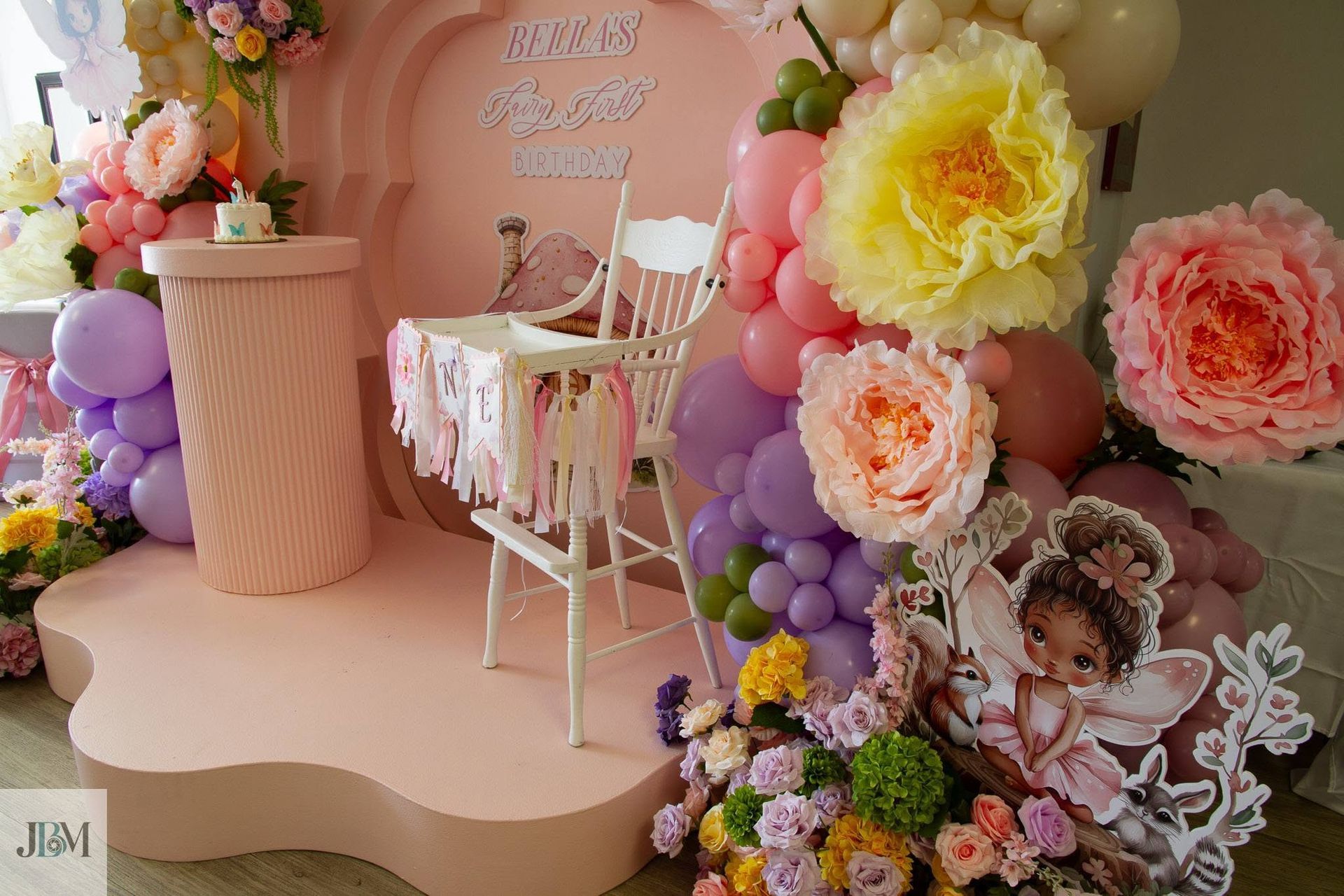 Pastel baby shower display with floral chair, giant paper flowers, balloons, and teddy bear decor