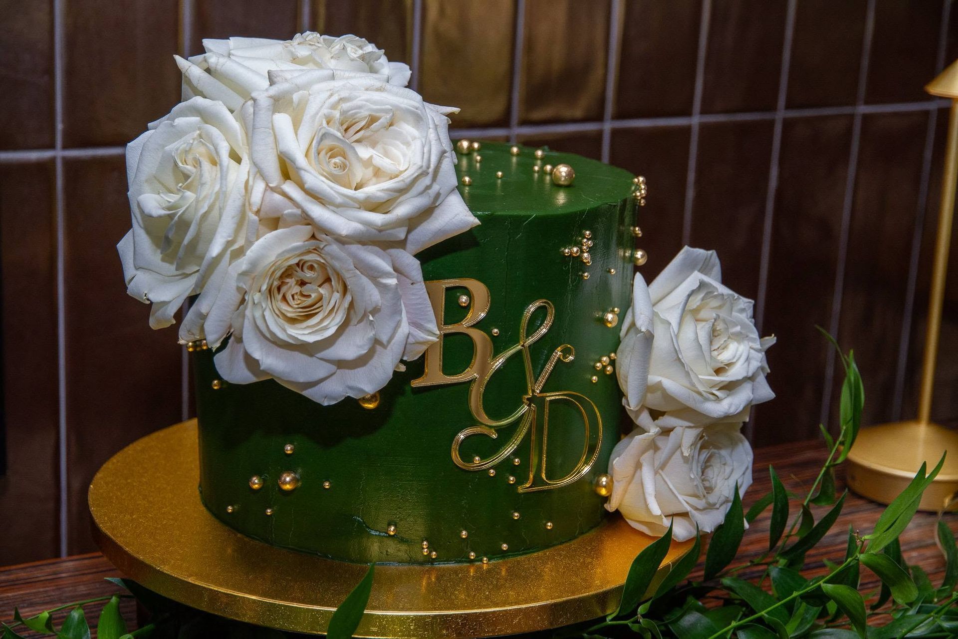 Green tiered cake with white roses and gold lettering on a gold cake board