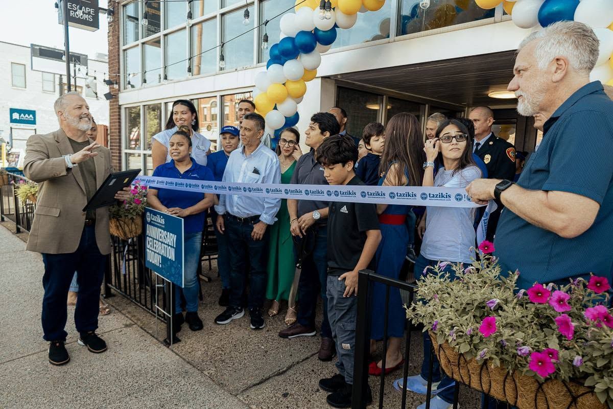 Ribbon cutting outside a building with a crowd, balloons, and two people holding the ribbon ends