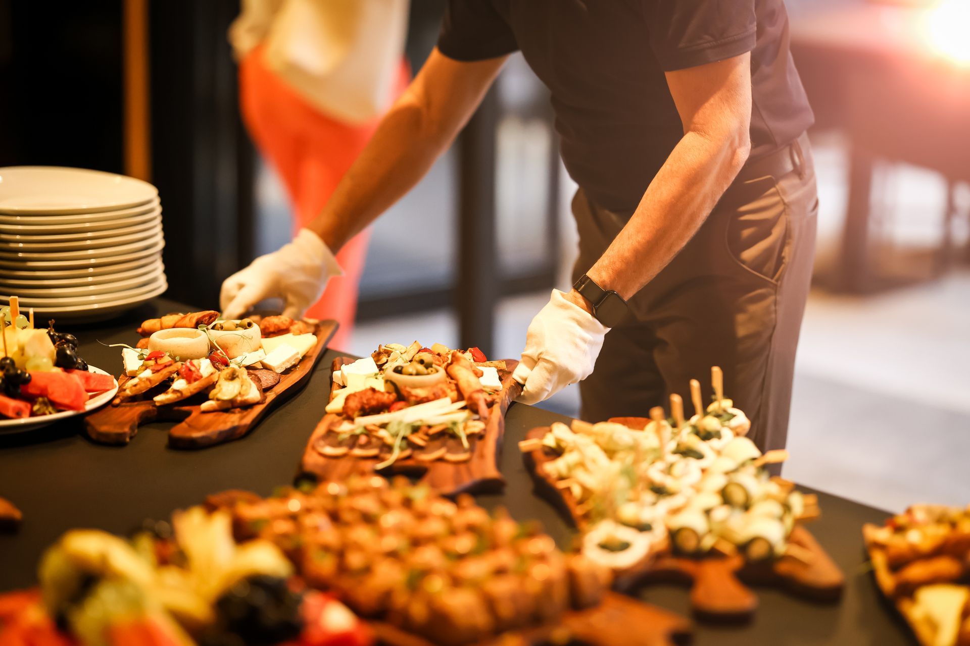 Person arranging appetizers on a buffet table in a warm-lit catering setting