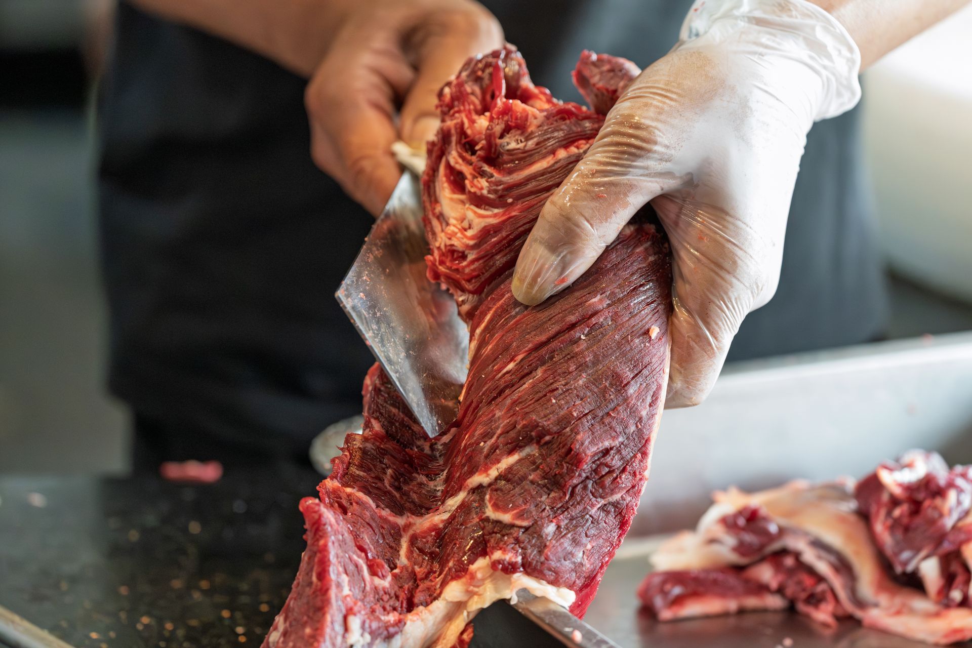 Gloved hands cutting raw meat on a butcher’s counter with a cleaver