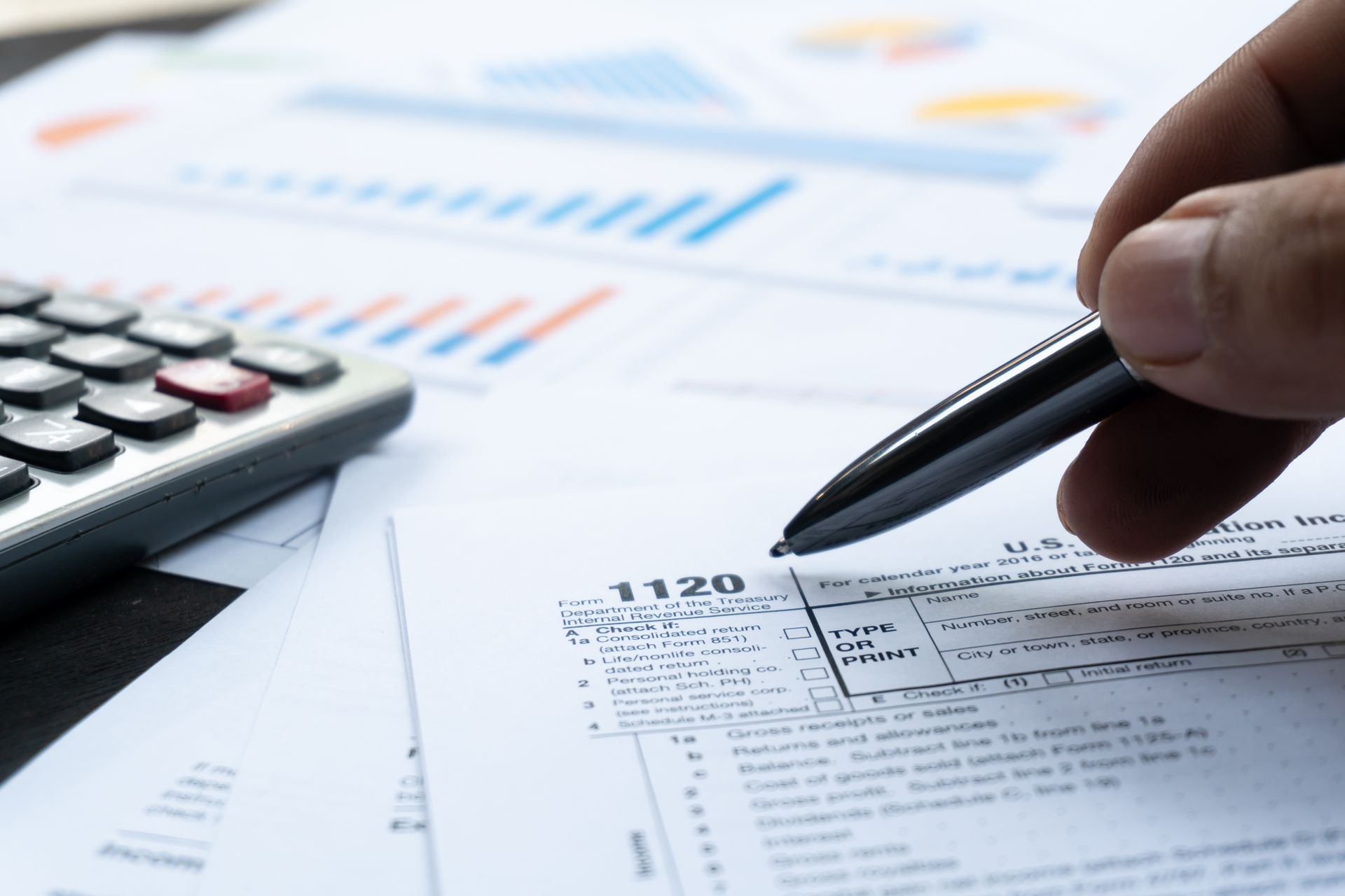 Hand with pen pointing at a 1120 tax form