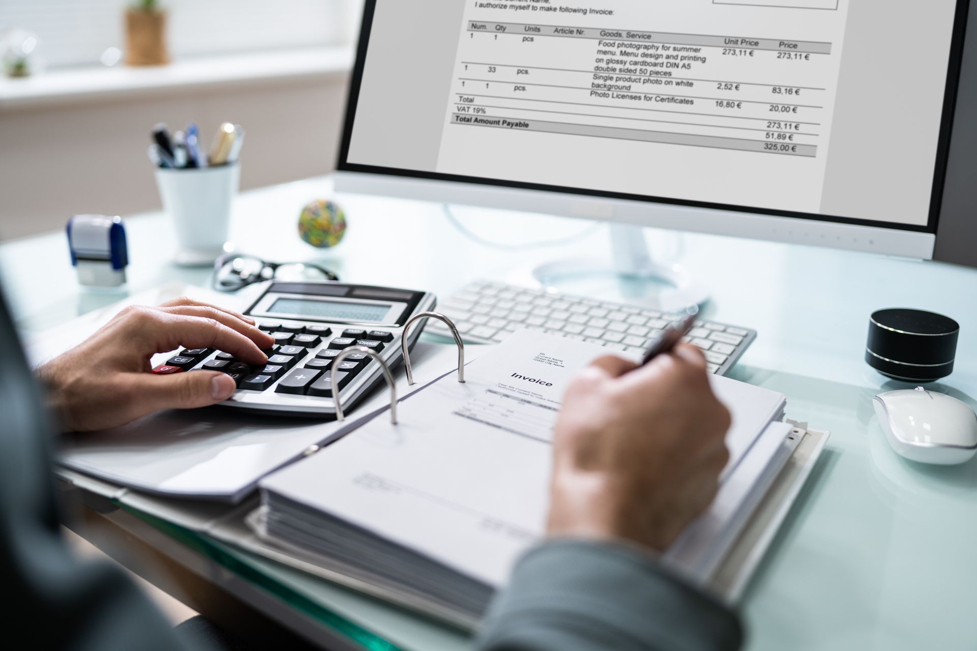 Person calculating with a calculator and reviewing an invoice on a computer